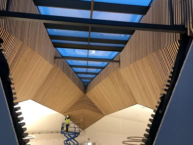 Montering av akustiske trepaneler med glassfelt i kontorbygg.